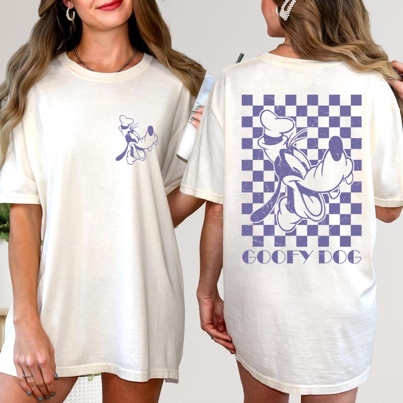Puede incluir: Camiseta color crema con una imagen de dibujos animados p&uacute;rpura de Goofy en la parte delantera y trasera. El dise&ntilde;o trasero incluye un patr&oacute;n de cuadros y las palabras "GOOFY DOG". La camiseta tiene mangas cortas y un corte holgado.