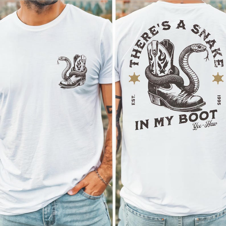 Puede incluir: Una camiseta blanca con un peque&ntilde;o gr&aacute;fico negro en el pecho izquierdo que muestra una serpiente enroscada alrededor de una bota vaquera. La parte trasera muestra una versi&oacute;n m&aacute;s grande del mismo gr&aacute;fico con el texto "THERE'S A SNAKE IN MY BOOT" y "EST. 1995".