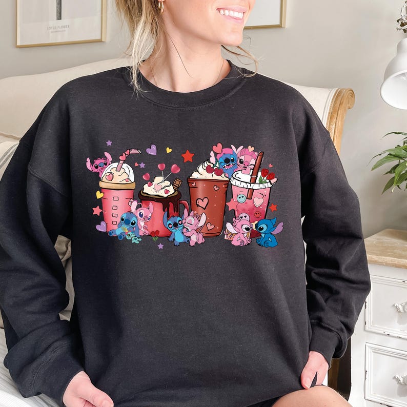 May include: Dark gray sweatshirt featuring a colorful graphic of cartoon characters with coffee drinks. The design includes pink, blue, and brown cups with whipped cream, hearts, and stars. The characters are in various poses around the drinks.