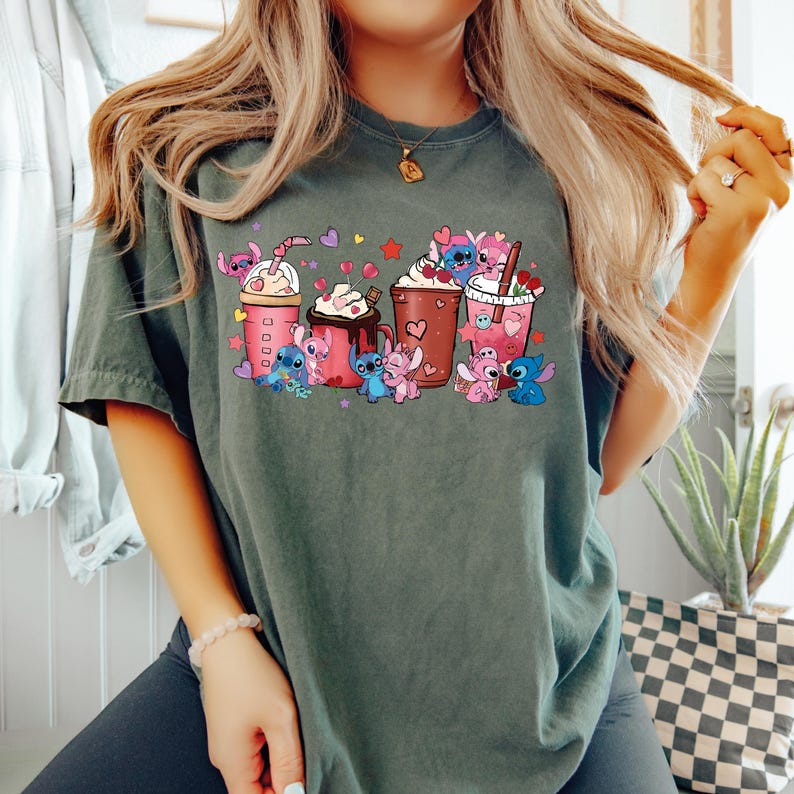 May include: Dark green t-shirt featuring a colorful graphic of cartoon characters with various beverages. The design includes pink, blue, and brown drinks with whipped cream and hearts. The shirt is a casual style.