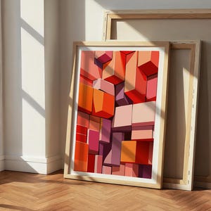 May include: Framed abstract art print featuring a geometric design of stacked blocks in shades of red, orange, and pink. The artwork is displayed in a light wood frame, leaning against a wall and another unframed canvas.