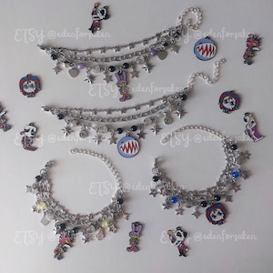 May include: Four silver-toned multi-strand charm bracelets featuring various metal star, spiral, and heart charms, black and coloured beads, and enamel character pendants. Several loose enamel character charms are scattered around the bracelets.
