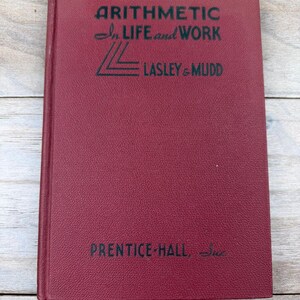 May include: A maroon hardcover book titled "Arithmetic in Life and Work" by Lasley & Mudd, published by Prentice-Hall. The book has a textured cover and black lettering.
