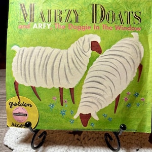 May include: Vintage vinyl record cover titled "Mairzy Doats and Arfy the Doggie in the Window." The cover features two white sheep with red heads and legs on a green background with flowers. A golden record label is visible.