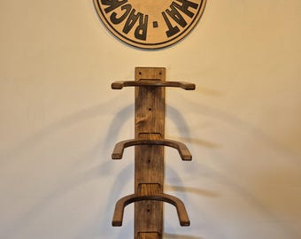 May include: A wooden hat rack with three curved hat holders. Above the rack is a circular wooden sign with the text "Oklahoma Hat Rack" and an American flag. The rack is mounted on a light-colored wall.