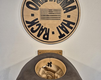 May include: A wooden sign with the words "OKLAHOMA HAT RACK" and an American flag design. Below the sign is a gray cowboy hat displayed on a wooden hat rack. The hat has a gold satin lining.