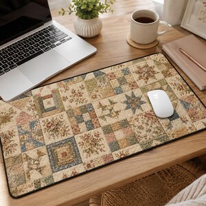 May include: A rectangular desk mat featuring a patchwork quilt design with various square blocks in muted tones of beige, blue, green, and pink. The pattern includes floral motifs, geometric shapes, and star patterns with a black stitched border.