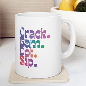 May include: White ceramic mug with the words "Crack. Bam. Pot. Sip." in a colorful, stacked design. The mug sits on a beige coaster. The mug has a curved handle and is suitable for hot or cold beverages.