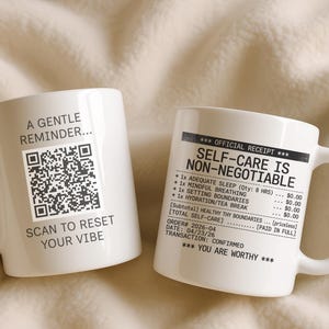 May include: Two white ceramic mugs. One mug has a QR code and the text "A GENTLE REMINDER... SCAN TO RESET YOUR VIBE". The other mug has a receipt design with the text "SELF-CARE IS NON-NEGOTIABLE" and "YOU ARE WORTHY".