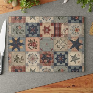 May include: Rectangular cutting board with a patchwork design. The board features a variety of squares with floral, star, and geometric patterns in shades of blue, red, and beige. A stainless steel knife is visible on the left.
