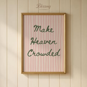 Puede incluir: Una impresión enmarcada con un marco dorado. La obra de arte presenta un fondo a rayas rosas y blancas con las palabras "Make Heaven Crowded" en letras cursivas verdes. La impresión se muestra en una pared de madera de color claro.