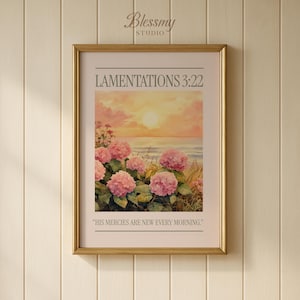 May include: A framed art print featuring a watercolor painting of pink hydrangeas in front of a sunset over the ocean. The text "LAMENTATIONS 3:22" and "HIS MERCIES ARE NEW EVERY MORNING" are displayed on the print. The frame is gold.