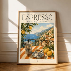 Könnte beinhalten: Ein gerahmter Kunstdruck mit dem Titel ESPRESSO Made in Italy, buon appetito! zeigt eine Küstenszene mit einem Espressokocher, einer Kaffeetasse auf einer Untertasse und Zitronen auf einem gestreiften Tisch vor einer Stadt am blauen Meer.