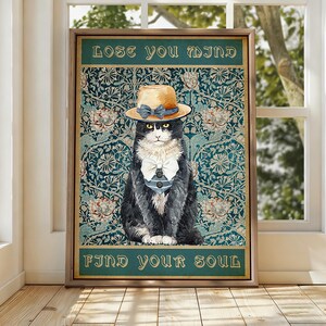 Könnte beinhalten: Ein gerahmter Kunstdruck mit einer schwarz-weißen Katze, die einen beigen Strohhut mit blauem Band und eine weiße Fliege trägt. Der Hintergrund zeigt ein florales Muster in Petrol. Der Text lautet LOSE YOU MIND oben und FIND YOUR SOUL unten.