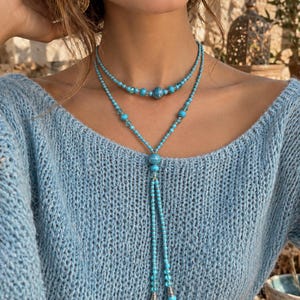 Può includere: Una collana a più fili con perline color turchese e piccoli distanziatori color argento. Il design include un filo più corto in stile girocollo e un filo più lungo che scende a cravatta con due estremità rifinite da terminali argentati.