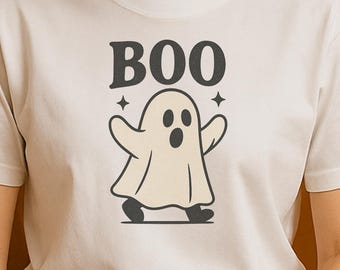 May include: White t-shirt featuring a cartoon ghost with the word "BOO" above it. The ghost has outstretched arms and is standing on a black line. The design is in a vintage style, perfect for Halloween.