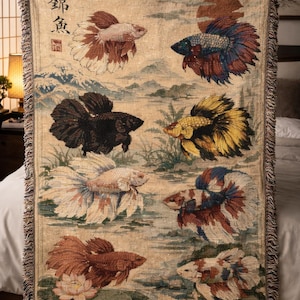 May include: Woven throw blanket featuring a repeating pattern of colorful betta fish in various poses. The background depicts a serene landscape with mountains and water. The blanket has a fringed edge and Japanese text.