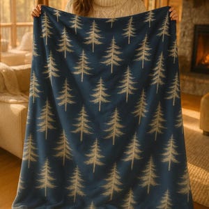 May include: A navy blue blanket with a repeating pattern of beige pine trees. The blanket is made of a soft material and is displayed indoors. The blanket is a cozy home decor item.