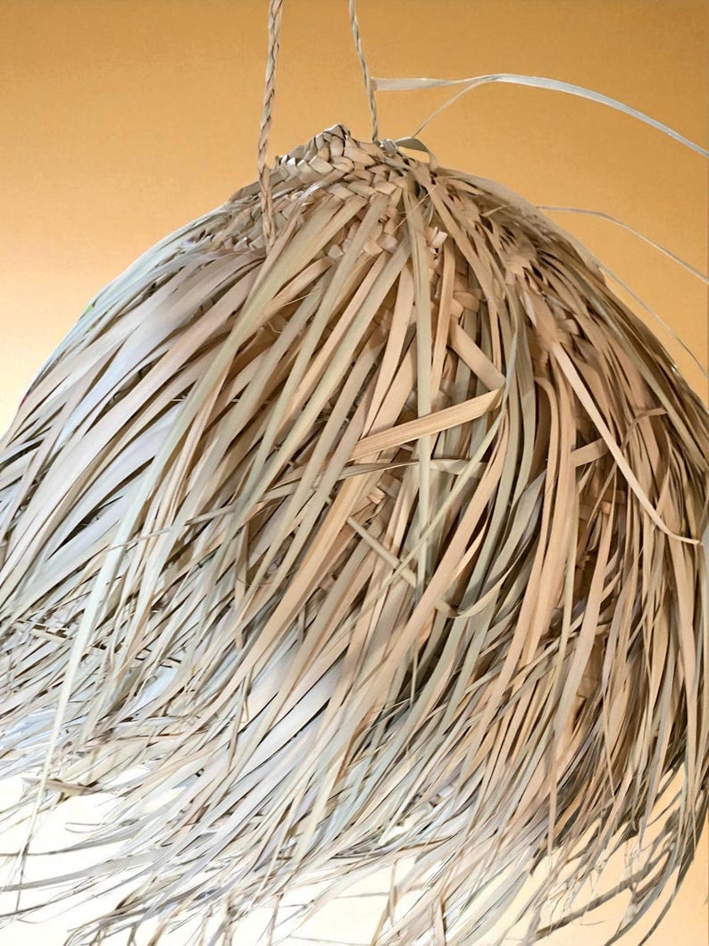 Puede incluir: L&aacute;mpara colgante artesanal hecha con hojas de palma secas, creando una pantalla texturizada. La l&aacute;mpara se suspende de una cuerda trenzada. El dise&ntilde;o evoca un estilo tropical o bohemio, con un enfoque en materiales naturales.