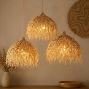 Puede incluir: Tres l&aacute;mparas colgantes con pantallas de rafia tejida natural cuelgan del techo. Las pantallas tienen un borde con flecos y est&aacute;n iluminadas desde dentro, proyectando un brillo c&aacute;lido. El tema general es bohemio y natural.