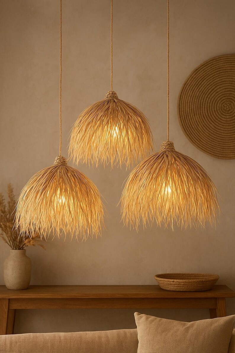 Puede incluir: Tres l&aacute;mparas colgantes con pantallas de rafia tejida natural cuelgan del techo. Las pantallas tienen un borde con flecos y est&aacute;n iluminadas desde dentro, proyectando un brillo c&aacute;lido. El tema general es bohemio y natural.