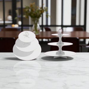 May include: Two white tiered serving stands on a marble surface. One stand has three tiers, the other has four. The stands are designed for displaying desserts or appetizers. A vase of flowers is in the background.