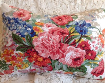 May include: A white pillow with a floral pattern featuring pink, red, yellow, and blue flowers. The pillow is made of a soft, cotton fabric and has a subtle sheen.