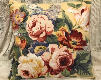 May include: A yellow throw pillow with a floral pattern featuring large pink, red, and yellow roses, green leaves, and a light purple flower.