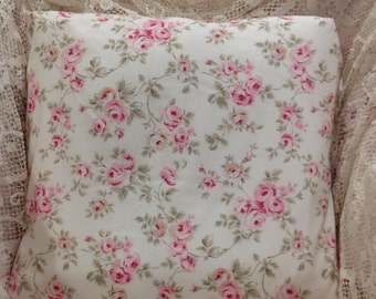 Può includere: Un cuscino bianco con un motivo floreale rosa e verde. Il cuscino è rivestito di un tessuto con un motivo ripetuto di piccole rose rosa e foglie verdi.