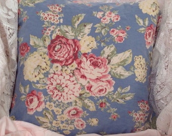 May include: A blue pillow with a floral pattern featuring pink, red, and yellow roses. The pillow is made of a soft, cotton fabric and has a subtle sheen.