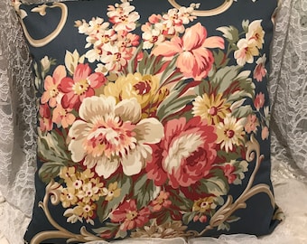 May include: Square throw pillow with a dark teal background and a large floral pattern. The flowers are in shades of pink, red, yellow, and cream, with green leaves. The pillow has a decorative gold scroll design.