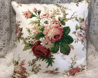 May include: Square throw pillow with a white background and a floral pattern. The pattern features large, detailed roses in shades of red, pink, and white, with green leaves and stems. The pillow is likely made of a soft fabric.