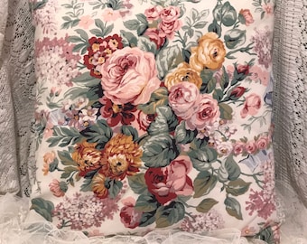 May include: Square throw pillow with a floral pattern. The pillow features a cream background with a large bouquet of roses in shades of pink, red, and yellow, with green leaves. The pillow is a decorative item.
