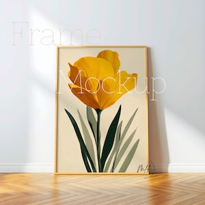 May include: A framed art print featuring a large yellow flower with green leaves against a cream background. The artwork is in a gold frame and leans against a white wall on a wooden floor. The word "Frame" and "Mockup" are written on the image.