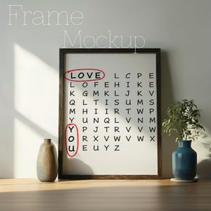 May include: A framed print with the words "LOVE YOU" circled in red. The print is a word search puzzle with the words "LOVE" and "YOU" highlighted. The frame is dark brown, and the print is displayed on a wooden surface.