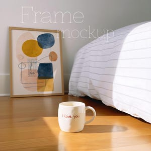 May include: A framed abstract art print with yellow, blue, and peach shapes. A white mug with "I love you" in red lettering sits on a wooden floor. The words "Frame mockup" are in the background.