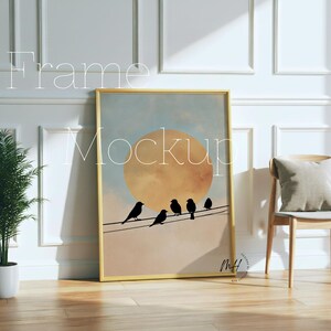 May include: A framed art print featuring a sunset scene with black bird silhouettes perched on a wire. The artwork has a gold frame and is leaning against a white wall. The word "Frame" and "Mockup" are written on the image.
