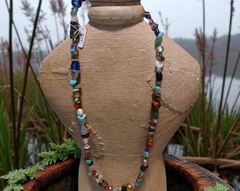 May include: A colorful beaded necklace with a variety of shapes and sizes of beads. The necklace is displayed on a tan mannequin. The beads include turquoise, red, blue, and black. A matching bracelet is at the top.
