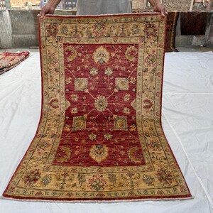 Könnte beinhalten: Ein rechteckiger, handgeknüpfter Teppich mit zentralem Medaillon-Design. Der Teppich hat ein tiefrotes Feld mit aufwendigen Blumenmustern in Beige und Gold. Der Rand ist beige mit floralen Motiven. Der Teppich ist ca. 183 cm x 274 cm groß.