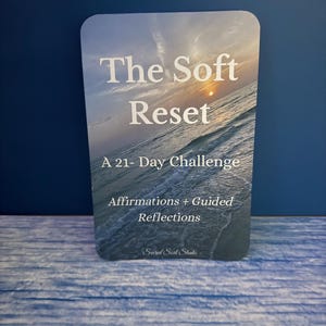 Może przedstawiać: Karta z zaokrąglonymi rogami z obrazem krajobrazu morskiego z tekstem "The Soft Reset" i "A 21-Day Challenge". Dodatkowy tekst zawiera "Affirmations + Guided Reflections" i "Sacred Soul Studio". Karta jest na niebieskim tle.