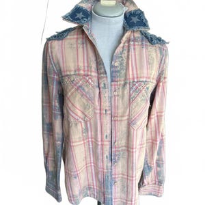 Peut inclure: Chemise à carreaux rose et beige à manches longues et deux poches de poitrine. La chemise a un aspect vieilli avec des accents bleus et des écussons en denim en forme d'étoile sur le col et les épaules. La chemise est boutonnée.