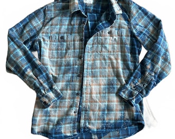 Può includere: Camicia di flanella a quadri blu e marrone con due tasche sul petto. La camicia button-down a maniche lunghe ha un colletto classico e polsini con bottoni. La camicia è realizzata in un tessuto morbido e strutturato.