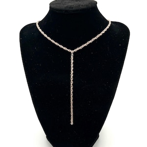 Könnte beinhalten: Eine zarte Halskette aus Roségold mit Y-förmigem Design. Die Halskette wird auf einer schwarzen Samtbüste präsentiert, die ihre feine Kette und den Anhänger-Tropfen zeigt. Der Schmuck ist vor einem weißen Hintergrund platziert.