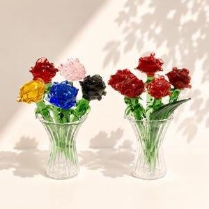 以下が含まれることがあります： 手作りのガラス製のバラが入った2つの透明なガラスの花瓶。左の花瓶には黄色、赤、薄いピンク、青、黒のバラが入っています。右の花瓶には、緑色のガラスの茎と葉が付いた3本の赤いバラが入っています。それぞれのバラには詳細な花びらがあります。