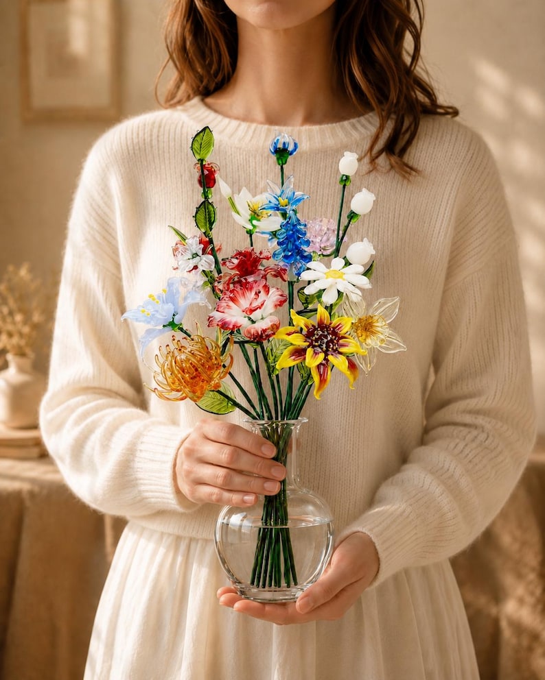 以下が含まれることがあります： 赤、黄、青、白など様々な色の手作りガラスの花束が入った透明なガラスの花瓶。茎は緑色で細く、花には複雑な花びらのディテールとガラスの葉が施されています。
