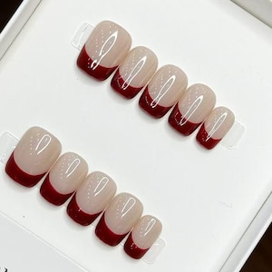 May include: A set of artificial nails with a French manicure design. The nails are a light beige color with a deep red tip. The set is displayed in a white box with the text "HANDMADE NAIL" and the number "19842".