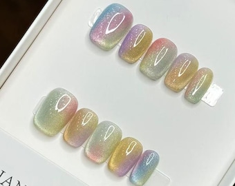 May include: A set of iridescent press-on nails in a white box. The nails have a rectangular shape and a shimmering, multi-colored finish, with hues of pink, yellow, green, and blue. The box has the text "HANDMADE NAIL" and the number "19735".