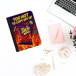 May include: A notebook with a purple cover featuring a Takis Fuego bag design with flames and the text "TOO HOT TO COPY OFF OF." The notebook is surrounded by office supplies, including a laptop, pink notebook, and gold accessories.