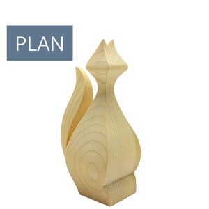 Könnte beinhalten: Eine Holzskulptur eines stilisierten Fuchses mit gebogenem Schwanz und spitzen Ohren. Der Fuchs ist aus hellfarbenem Holz gefertigt und hat eine glatte Oberfläche. Das Wort "PLAN" befindet sich in einem blauen Rechteck oben links.