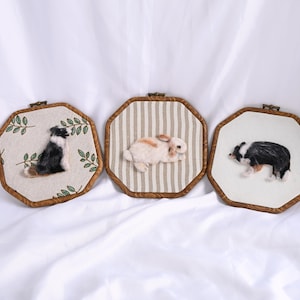 May include: Three framed felted animal portraits. One features a black and white dog with a brown patch, another a brown and white rabbit, and the third a black and white dog. Each is set in a wooden frame.